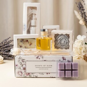May include: A gift set featuring a white box labeled SCENTS OF GLOW with floral patterns, containing a spray bottle, a rectangular soap with dried petals, a glass bottle of yellow oil, a flower-shaped candle, reed sticks, and purple wax melts.