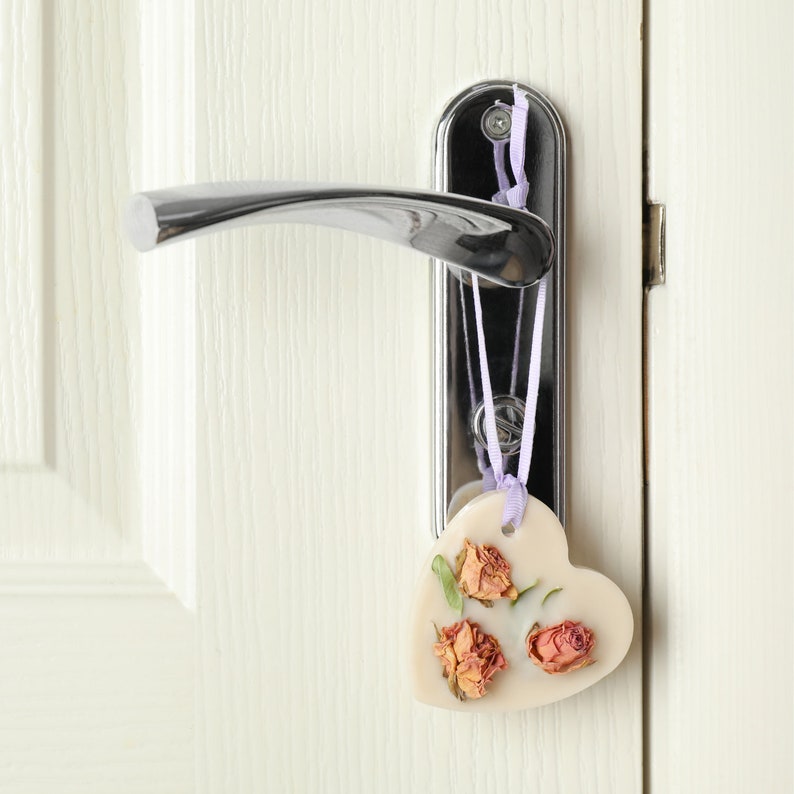 Puede incluir: Un coraz&oacute;n de cera blanco con rosas secas colgando de un pomo de puerta plateado.