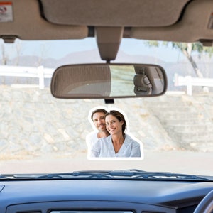 May include: A photo of a couple in a car. The couple is smiling and looking at the camera. The photo is attached to the rearview mirror of the car.