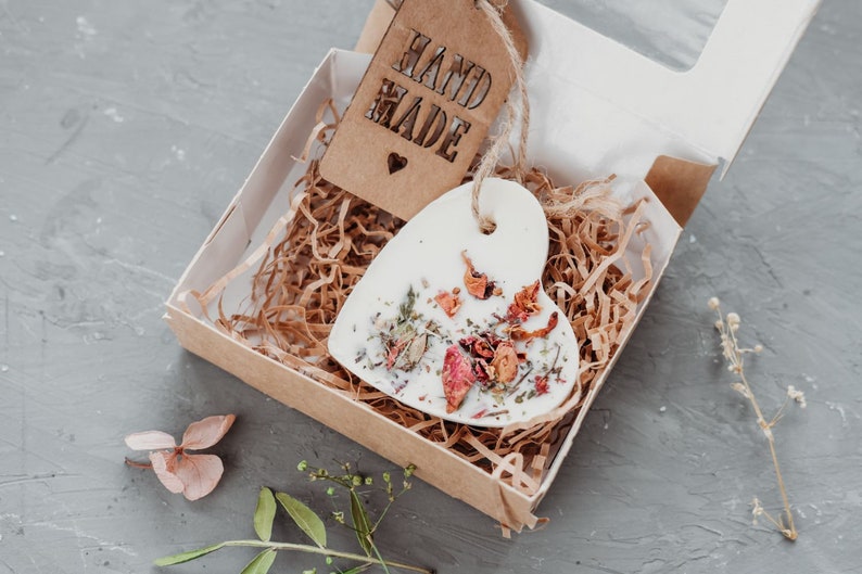 Puede incluir: Un adorno de cer&aacute;mica blanco en forma de coraz&oacute;n con flores y hierbas secas en su interior, empaquetado en una caja marr&oacute;n con una etiqueta "Hand Made".