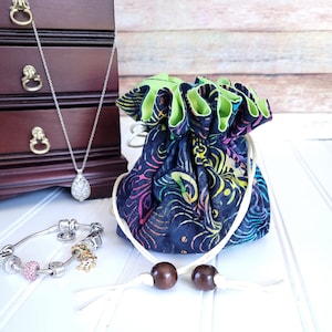May include: A black and green drawstring bag with a colorful floral pattern. The bag has a white drawstring with brown wooden beads. A silver necklace with a teardrop pendant and a silver charm bracelet with colorful charms are also pictured.