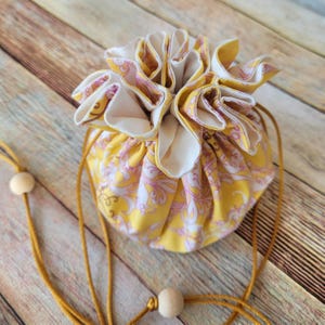May include: A yellow drawstring bag with a white and pink floral pattern. The bag is gathered at the top and has a yellow drawstring.