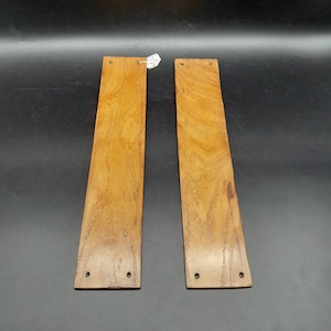 May include: Two wooden door pulls with a brown stain finish. Each pull has two holes for mounting.