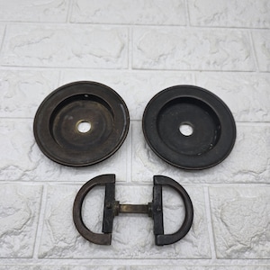 May include: Three antique metal hardware pieces. Two circular pieces with a central hole and a D-shaped handle with a connecting bar. The hardware has a dark, aged finish.