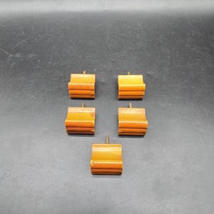 May include: Five vintage wooden furniture feet with a warm, amber finish. Each foot has a rectangular shape with horizontal grooves and a screw for attachment. The feet are arranged against a dark background.
