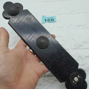 May include: Black wooden door plate with two round knobs and a decorative design at each end. The plate has a worn, aged look.