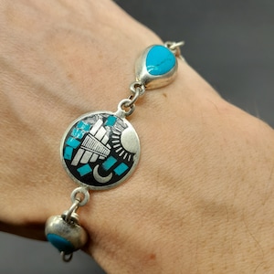 Könnte beinhalten: Ein silbernes Armband mit Türkis-Steinen und einem runden Anhänger mit Sonne, Mond und geometrischem Muster.