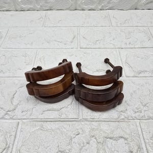 May include: Two sets of wooden cabinet pulls. Each set includes three curved, dark brown pulls with mounting hardware. The pulls have a smooth, glossy finish and are arranged in a stack.