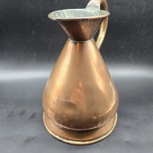 May include: A copper jug with a flared spout and a handle. The jug is marked "1/2 GALLON".