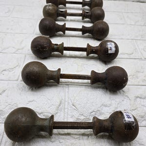 May include: A set of antique cast iron door knobs. Each knob features a rounded handle at each end of a rectangular bar. The knobs are a dark, rusty brown, with signs of age and wear. Some knobs have small white stickers with numbers.