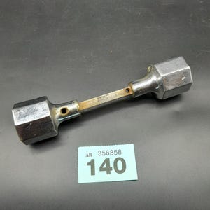 May include: A chrome-plated metal tool with two hexagonal ends and a narrow, rectangular shaft. The tool shows signs of wear. A small blue tag displays the number "140" and the text "AB 356858".