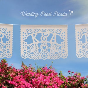 Puede incluir: Banderines de papel picado blancos con las letras K & A en el centro, colgando de un cielo azul. Los banderines est&aacute;n decorados con intrincados dise&ntilde;os florales. El texto "Wedding Papel Picado" est&aacute; escrito en blanco sobre los banderines.