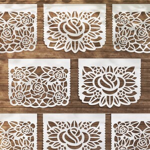 K&ouml;nnte beinhalten: Satz von acht wei&szlig;en Papierschnitten mit einem floralen Design. Jeder Schnitt zeigt eine Rose mit filigranen Details und einem gewellten Rand. Die Schnitte sind in einem Rastermuster auf einer Holzoberfl&auml;che angeordnet.