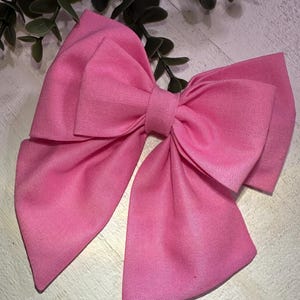 Könnte beinhalten: Eine große rosafarbene Schleife aus Stoff mit einer spitzen Form am unteren Ende jeder Schlaufe.