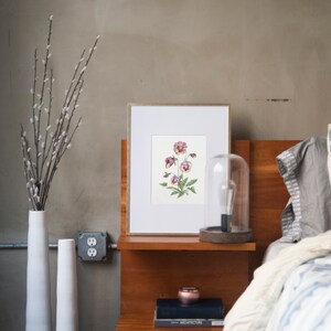 May include: A framed botanical print of purple and white pansies with green leaves on a white background. The print is on a wooden nightstand with a book and a small decorative object. There is a clear glass cloche with a light bulb on the nightstand.