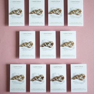 May include: Arrangement of soft enamel pins on white cards against a pink background. Each pin features a gold-colored design with white floral accents. The cards display the text "Sekindar Calligraphy" and "Soft Enamel Pin".