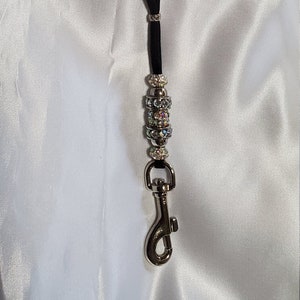 May include: A black lanyard with a silver clasp and a silver bead with iridescent rhinestones.