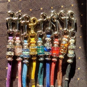 May include: A set of ten colorful, braided cords with silver clasps and crystal beads. Each cord has a different color and crystal bead design.