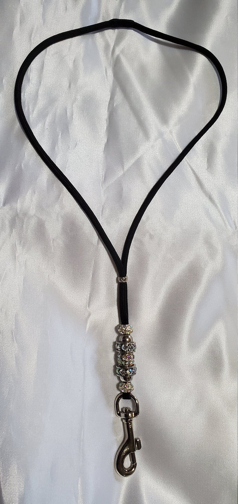 May include: A black lanyard with a silver clasp and a silver bead with iridescent rhinestones.