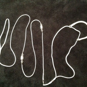 May include: White cord necklace with three silver beads. The cord is looped and knotted to create a unique design.