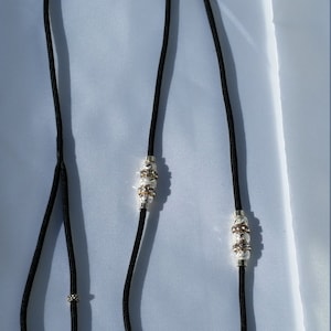 May include: A black paracord leash with silver and gold beads. The leash has a loop at one end and a slip knot at the other.