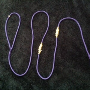 May include: A purple dog leash with two gold metal accents.