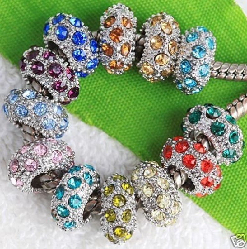 May include: A set of 10 colorful charm beads with crystal accents. Each bead is silver-toned and features a different color of crystals.