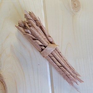 May include: A bundle of thin, light brown wood shavings tied together with a brown ribbon. The shavings are arranged in a fan shape.