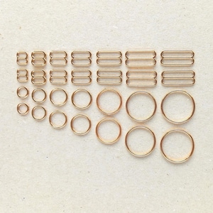 May include: A set of gold-toned metal rings and rectangular clasps. The rings are of various sizes and are arranged in a grid pattern. The clasps are all the same size and are arranged in a row above the rings.