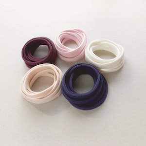 Pode incluir: Cinco carretéis de cordão de tecido em diferentes cores: bordô, rosa, branco, beige e azul marinho.