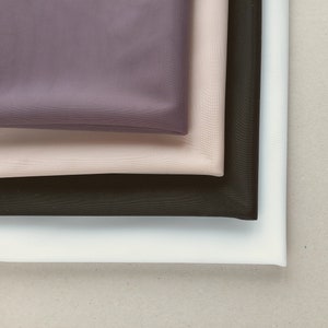 Può includere: Quattro pezzi di tessuto impilati uno sopra l'altro. Il pezzo superiore è di colore viola scuro, il secondo pezzo è di colore beige chiaro, il terzo pezzo è di colore nero e il pezzo inferiore è di colore bianco.