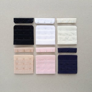 Può includere: Assortimento di prolunghe per spalline del reggiseno in vari colori e dimensioni. Le prolunghe sono realizzate in tessuto e hanno ganci e occhielli in metallo. I colori includono nero, bianco, beige, rosa e blu navy.