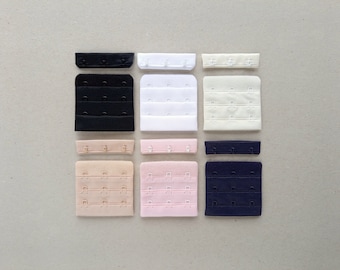 May include: Assortment of bra strap extenders in various colours and sizes. The extenders are made of fabric and have metal hooks and eyes. The colours include black, white, beige, pink, and navy blue.