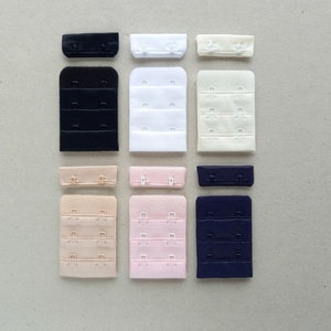 May include: Assortment of bra strap extenders in various colors, including black, white, beige, pink, and navy blue. The extenders have three rows of hooks and eyes.