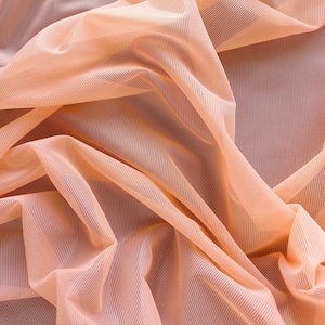 May include: Peach-colored sheer fabric with a fine mesh texture. The fabric is draped and folded, creating soft, flowing lines.