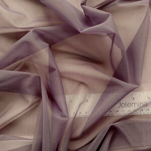 May include: A close-up of a sheer, mauve fabric with a subtle sheen. The fabric is draped and folded, creating soft, flowing lines. A ruler with the word "Jolemina" printed on it is visible in the bottom right corner.