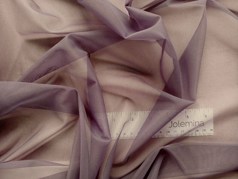 May include: A close-up of a sheer, mauve fabric with a subtle sheen. The fabric is draped and folded, creating soft, flowing lines. A ruler with the word "Jolemina" printed on it is visible in the bottom right corner.