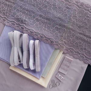 May include: A set of lilac-colored fabric scraps, lace trim, and elastic ribbon. There are also silver metal bra clasps and rings.
