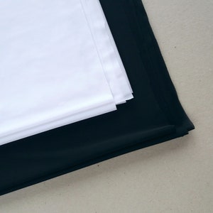 May include: A white fabric backdrop folded on top of a black fabric backdrop.
