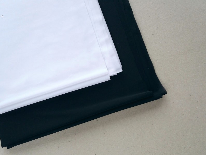 May include: A white fabric backdrop folded on top of a black fabric backdrop.