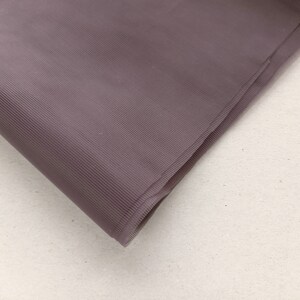 May include: A close-up of a folded piece of mauve tulle fabric. The fabric has a fine, woven texture.