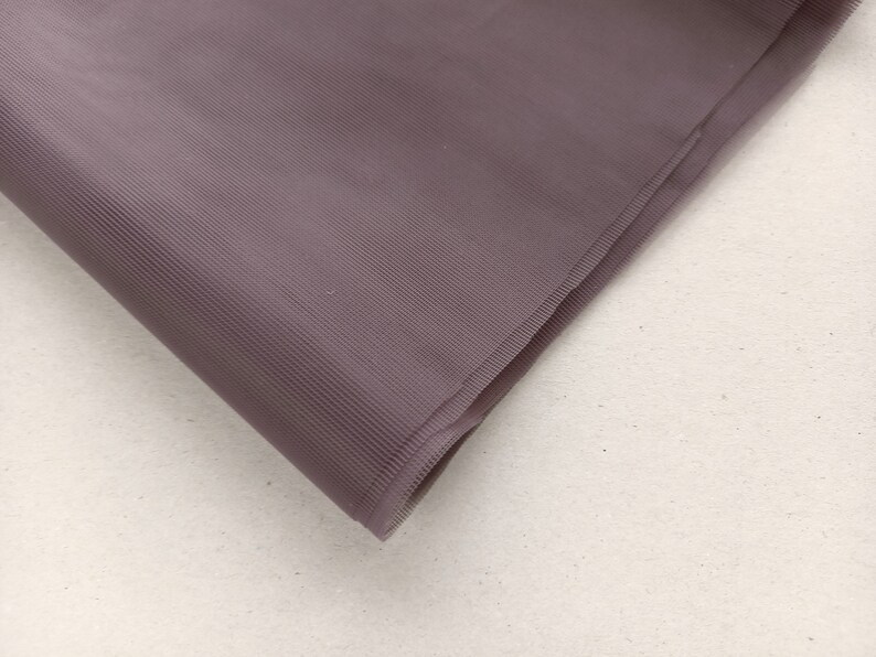 May include: A close-up of a folded piece of mauve tulle fabric. The fabric has a fine, woven texture.