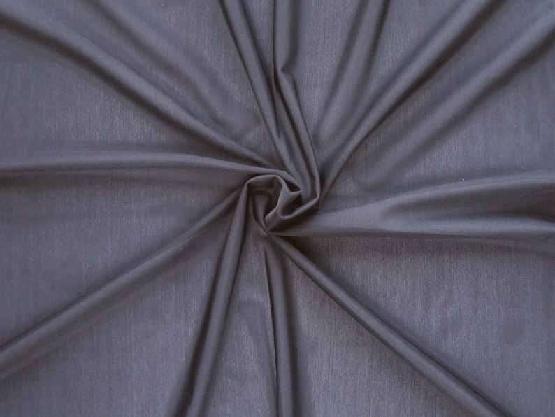 May include: A close-up of a smooth, dark gray fabric with a soft, flowing texture. The fabric is gathered in the center, creating a swirling pattern.