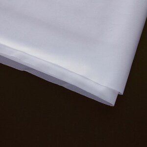 May include: White sheer fabric with a soft, delicate texture. The fabric is folded over on itself, creating a smooth, even edge.