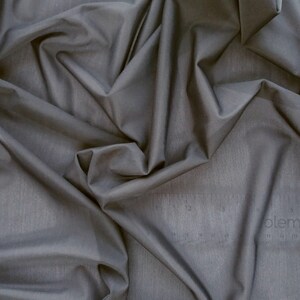 May include: A close-up of a smooth, dark gray fabric with a subtle texture. The fabric is draped and folded, creating soft, flowing lines.