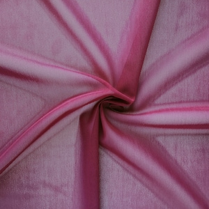 May include: A close-up of a soft, pink fabric with a subtle sheen. The fabric is draped and folded, creating a smooth, flowing texture.