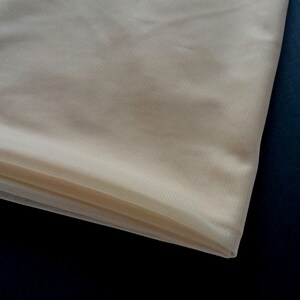 Puede incluir: Un trozo de tul transparente de color blanco roto. La tela est&aacute; doblada y tiene una textura suave y delicada.