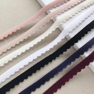 May include: Selection of elastic trim ribbons in shades of pale pink, cream, white, black, navy blue, and burgundy. Each ribbon has a scalloped edge. Ideal for sewing and craft projects.