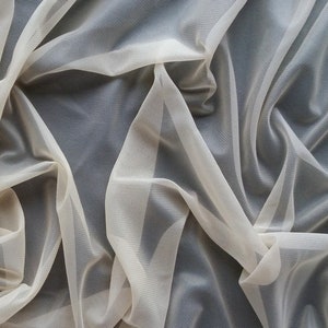 Puede incluir: Un trozo de tela de color marfil, fina y transparente, con una textura suave y fluida. La tela est&aacute; drapeada y doblada, creando un aspecto delicado y aireado.