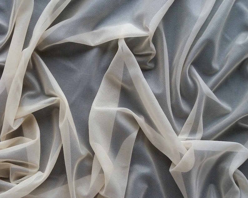 Puede incluir: Un trozo de tela de color marfil, fina y transparente, con una textura suave y fluida. La tela est&aacute; drapeada y doblada, creando un aspecto delicado y aireado.